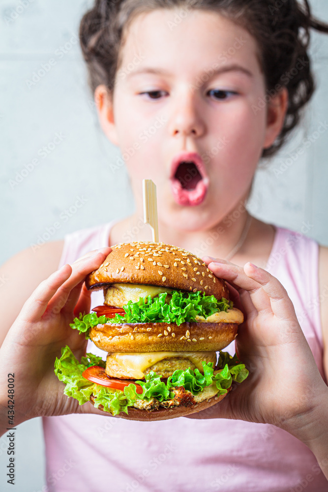 Brunette teenage girl eating big vegan burger.