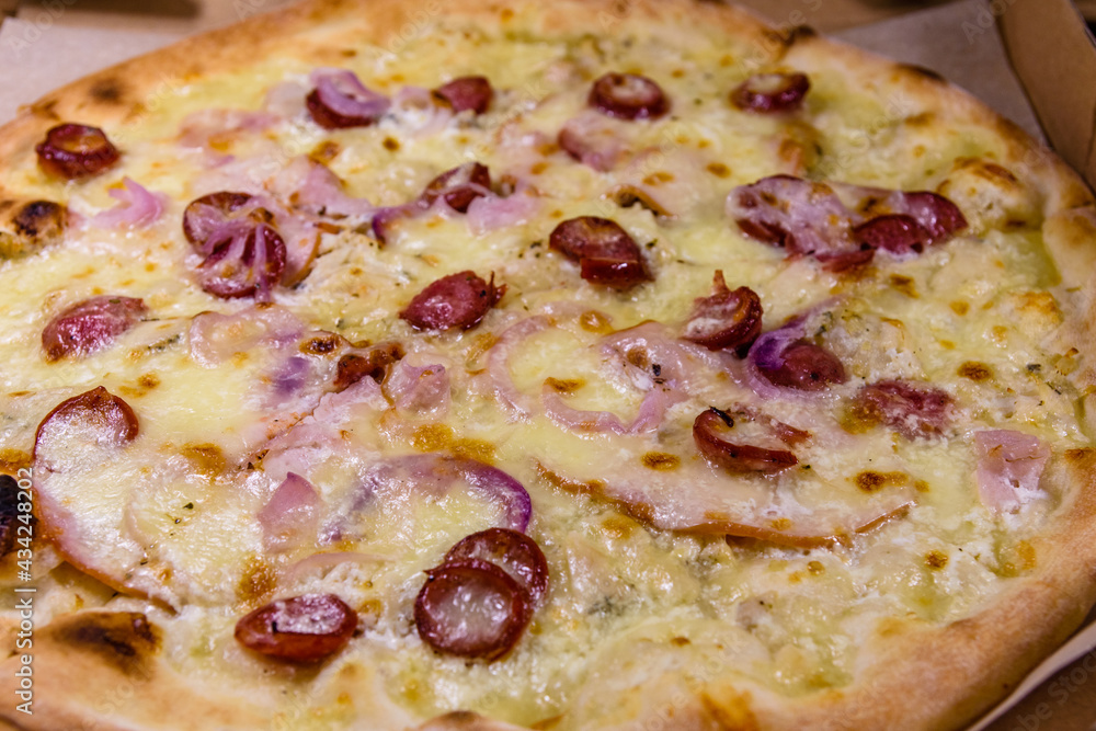Pizza with sausages, ham and parmesan cheese in cardboard box on a wooden table Pizza with sausages, ham and parmesan cheese in cardboard box on a wooden table