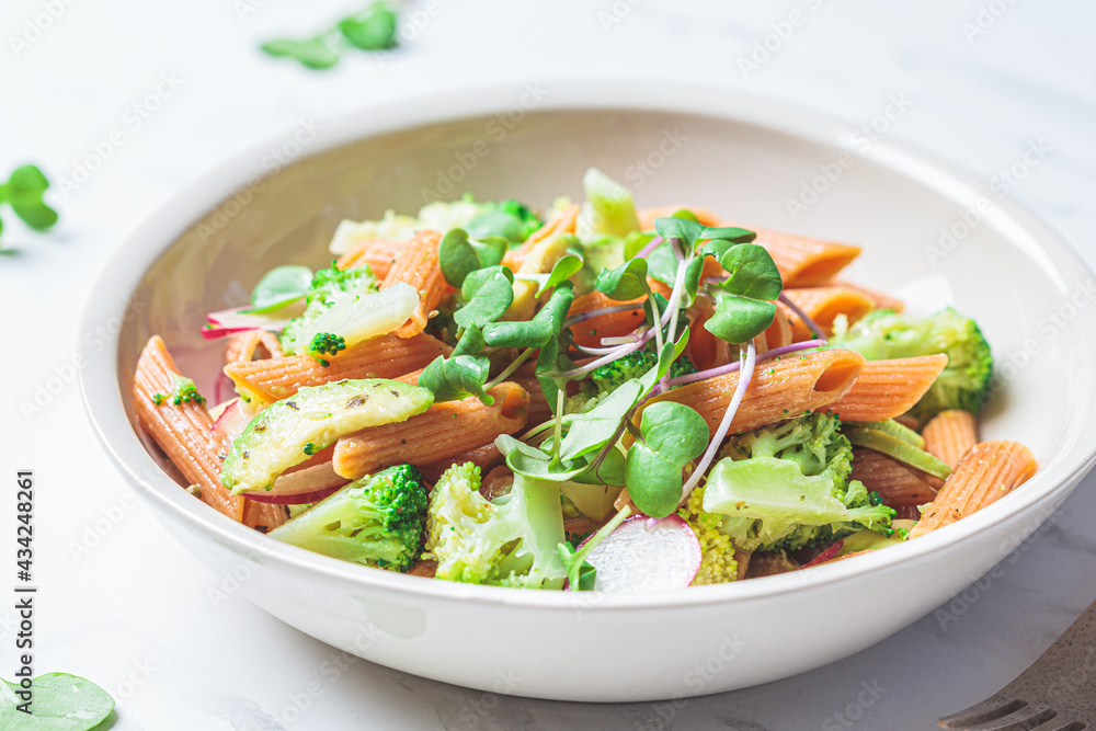 Lentil pasta with broccoli, avocado, radish and sprouts in white bowl. Healthy vegan recipe concept. Lentil pasta with broccoli, avocado, radish and sprouts in white bowl. Healthy vegan recipe concept.