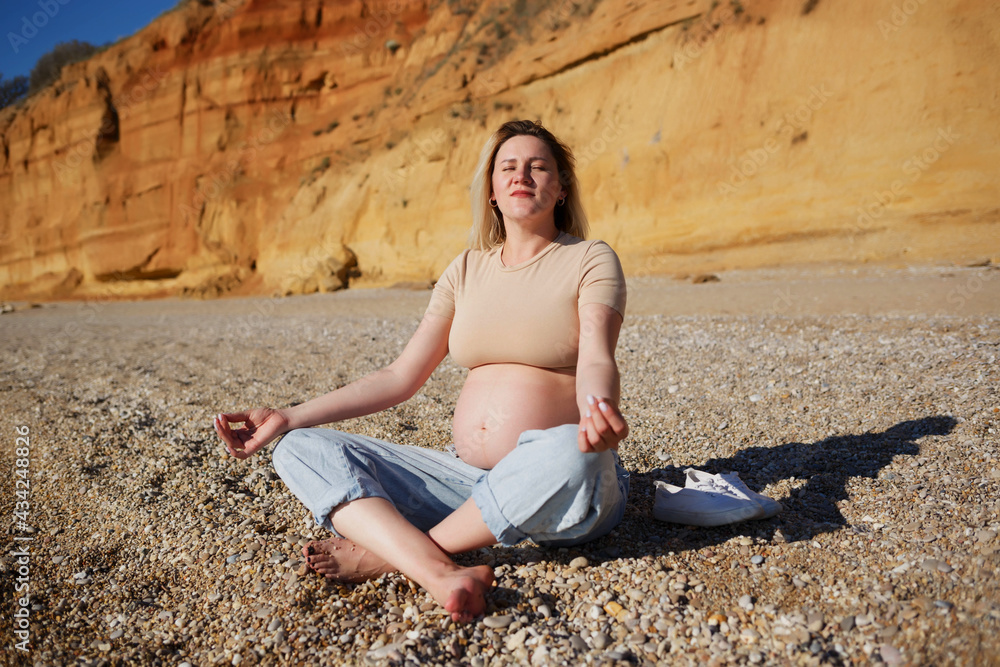 pregnant woman sitting on yellow rock and meditating