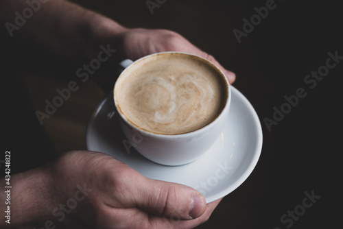 White cappuccino cup in the hands of a man