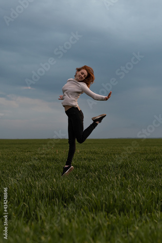 Portrait of cheerful positive girl jumping in the field against stormy sky