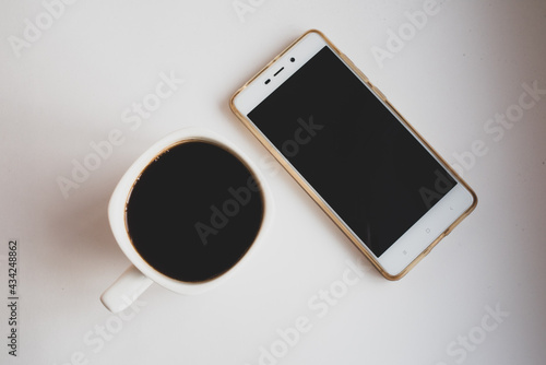 White mug with black coffee and white mobile phone