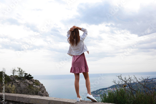 young woman stands over a cliff with her hands up