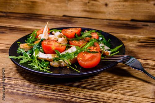 Roasted chicken breasts and salad with arugula and cherry tomatoes in a black plate