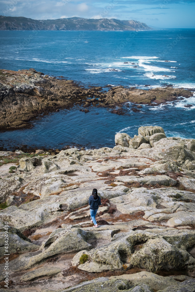 MALPICA, SPAIN - AUGUST 4, 2020: A girl walks along some rocks, near the Punta Nariga lighthouse.