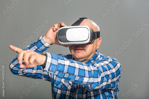 Old man in virtual reality glasses over grey background