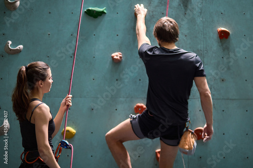 Female instructor giving instructions to man on wall climbing. man learning the art of rock climbing at an indoor climbing centre, wearing safety equipment