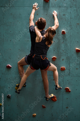fitness, extreme sport and healthy lifestyle concept. young couple bouldering on rock climbing wall at indoor gym, rear view on young man and woman engaged in sport, preparing for competition