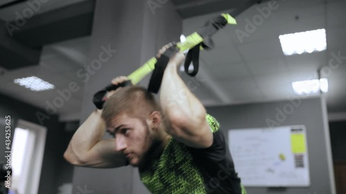 From below of focused strong male athlete doing exercises on TRX straps during suspension training in modern gym 