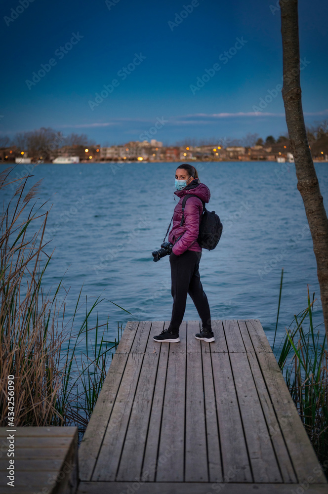 Young traveler girl on the walkway of the lake with a camera, it is night, blue hour