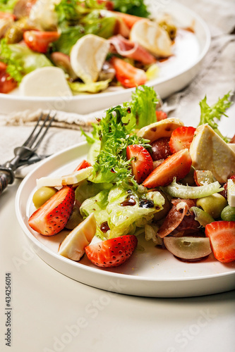 Close-up salad with jamon, strawberries, grapes, mozzarella and olives with pomegranate sauce. Healthy and balanced nutrition. Organic food. Mediterranean cuisine recipes. Vertical shot. Copy space