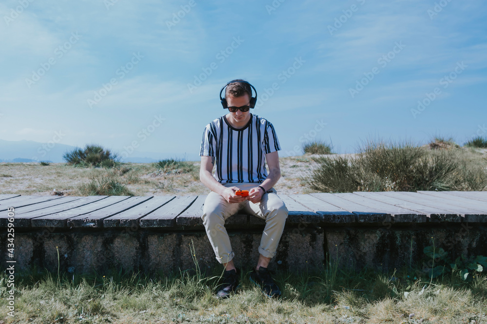 young man sitting with mobile phone and headphones listening to music young man sitting with mobile phone and headphones listening to music