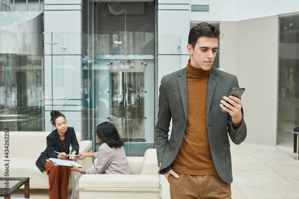 Fototapeta premium Young businessman using his mobile phone with two businesswomen communicating in the background