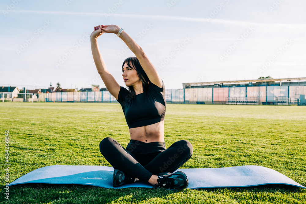 Fototapeta premium Beautiful young girl doing yoga outdoors on the grass during the sunny day. Healthy lifestyle concept.