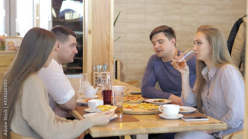 Friends are sitting in a cafe chatting, sharing lunch during a meeting, sitting at a cozy pizzeria table. Laughs while enjoying food and drinks together, and enjoys eating together. Double date Friends are sitting in a cafe chatting, sharing lunch during a meeting, sitting at a cozy pizzeria table. Laughs while enjoying food and drinks together, and enjoys eating together. Double date