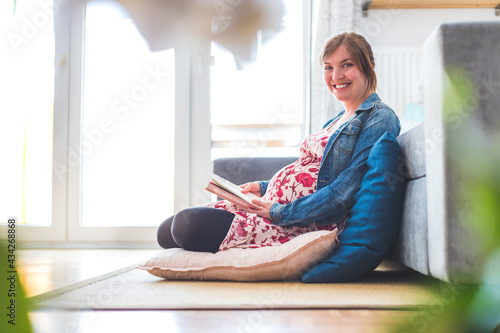Preparing for pregnancy: Pregnant Caucasian mother is sitting on the floor, reading a book for about babies