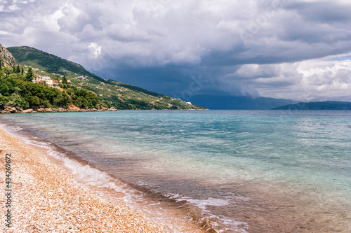 Beautiful landscape - turquoise colored sea water  golden sand  gray sky with dark stormy clouds and mountains on the horizon.