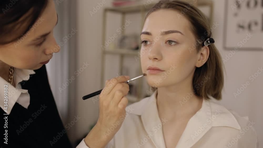 Crop professional visagiste applying decorative cosmetics on face of young woman. Anonymous makeup artist applying powder with brush on female client in beauty studio Crop professional visagiste applying decorative cosmetics on face of young woman. Anonymous makeup artist applying powder with brush on female client in beauty studio