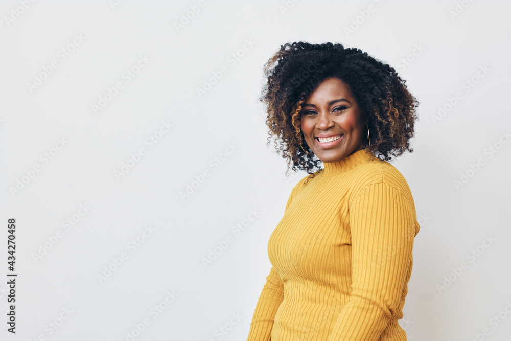 Studio portrait of cheerful mid adult black woman smiling at camera. Curly hair, yellow sweater, white background. Studio portrait of cheerful mid adult black woman smiling at camera. Curly hair, yellow sweater, white background.
