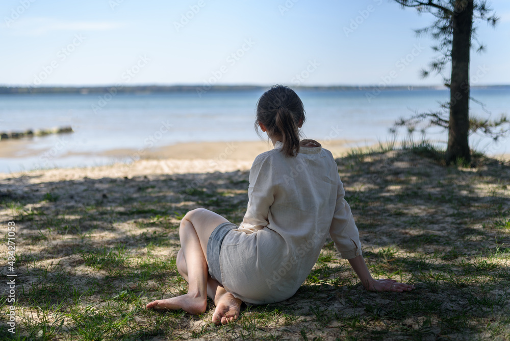 Woman in linen clothes sitting between pine trees and looking to sea. Wellbeing, mental health