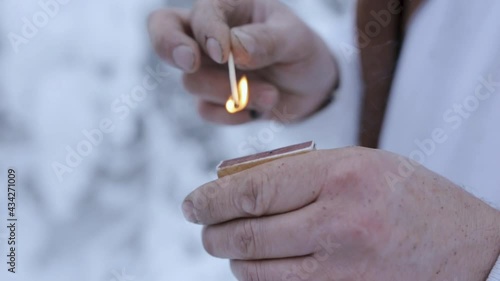 Closeup of crop male traveler lighting match in snowy forest in winter 