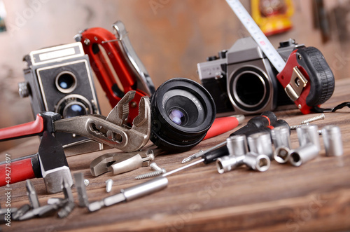 Analoge TLR und SLR Fotokameras mit unterschiedlichen Werkzeugen auf Holztisch vor Vintage Hintergrund liegend
