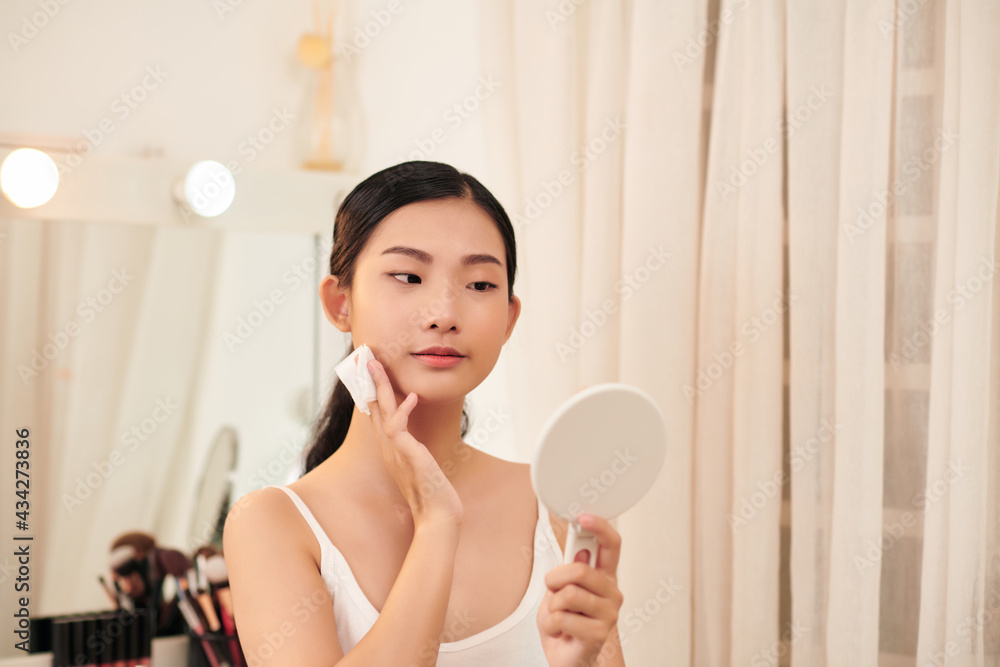 Young cute woman remove makeup , cleaning face with cotton pads looking in mirror Young cute woman remove makeup , cleaning face with cotton pads looking in mirror