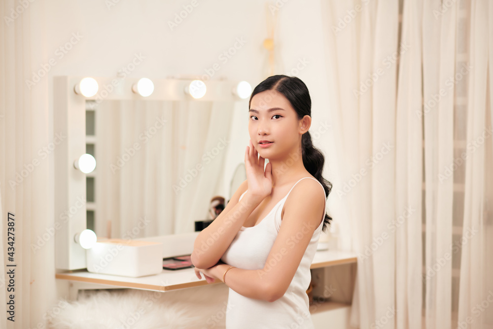 Taking off her make-up. Beautiful cheerful young woman using cotton disk and looking at her reflection in mirror with smile while sitting at the dressing table Taking off her make-up. Beautiful cheerful young woman using cotton disk and looking at her reflection in mirror with smile while sitting at the dressing table