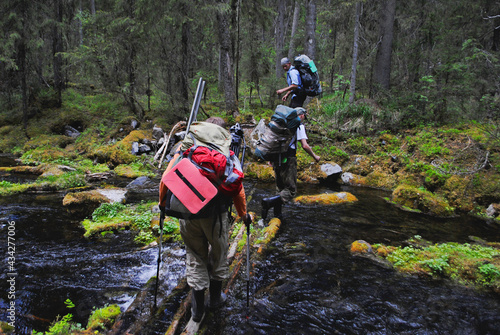 Men with backpacks cross the river in the forest