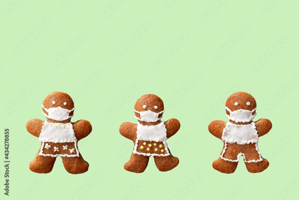 Fototapeta premium Cute gingerbread family with protective face masks, isolated, green background. Greeting card, copy space for text. Creative concept in coronavirus (COVID-19) time