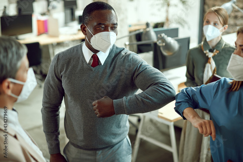 Business coworkers greeting with elbows and wearing protective face masks in the office due to COVID-19 pandemic.