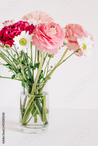 A bouquet of fresh spring flowers in a glass vase on a white table.