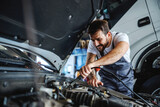 Hardworking dedicated bearded employee in overalls fixing motor. In background is truck. Manual jobs concept.