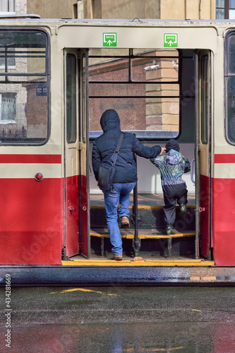 A man and a child walk through the open doors of public transport in the city