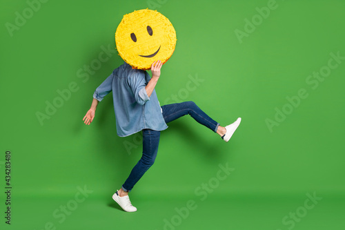 Full length body size side profile photo of man hiding face behind yellow smile isolated vivid green color background