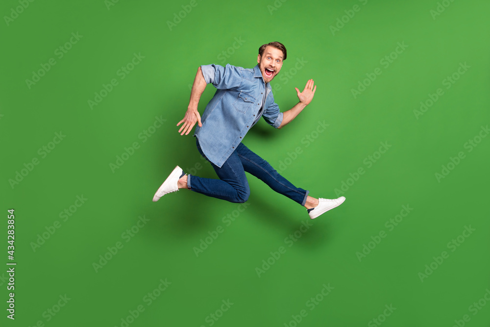 Full length body size side profile photo of young guy jumping up careless laughing isolated vibrant green color background Full length body size side profile photo of young guy jumping up careless laughing isolated vibrant green color background