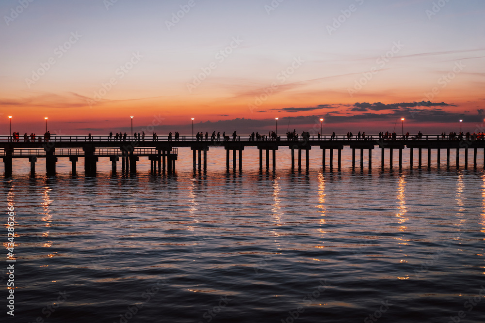 Sunset by the Baltic sea. Wooden bridge, lots of people in famous resort city Palanga, Lithuania, Europe.