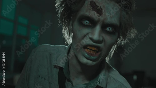 Close up shot of zombie man with SFX makeup with fake wounds and white contact lenses looking at camera and screaming in dark room with flashing lights