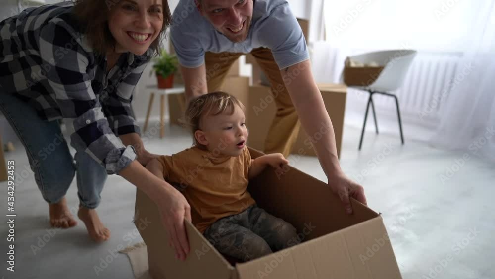 Young happy family in a new home rolls their child in a cardboard box on the floor. Real estate and mortgage concept Young happy family in a new home rolls their child in a cardboard box on the floor. Real estate and mortgage concept