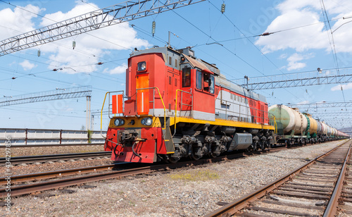 Freight locomotive pulls train with fuel tanks against blue sky.