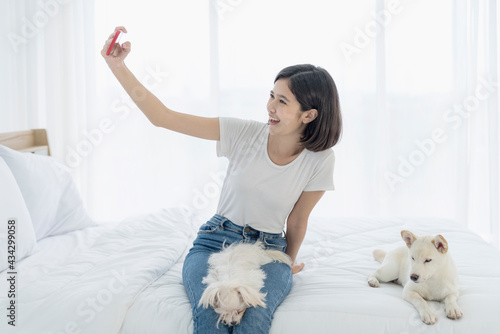 Fototapeta Naklejka Na Ścianę i Meble -  Young Asian women selfie with mobile phone. Young Asian women and girl were in bed with a dog. Girl and white Hokkaido inu dog and Maltese dog.