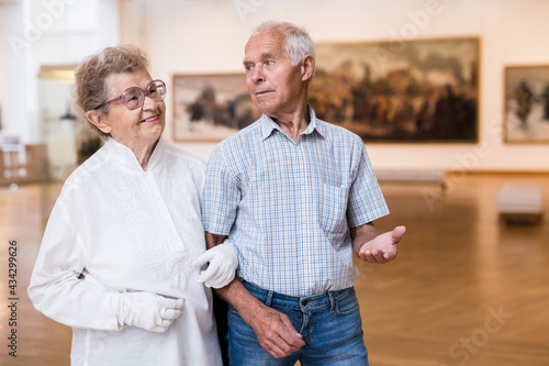 mature European couple examines paintings in an exhibition in hall of art museum