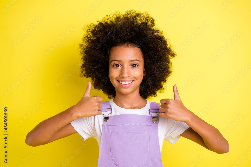 Photo of positive small girl raise thumb up look camera wear purple overall isolated yellow color background