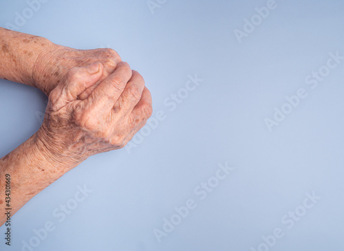 Close-up of senior woman's hands joined together for praying on a light blue background. Focus on hands wrinkled skin. Space for text. Concept of aged people and healthcare.