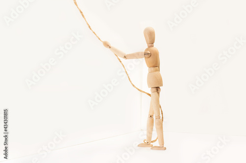 Muñeco maniqui de madera articulado con una soga en la mano subiendo un muro. Vista de frente y de cerca. Copy space