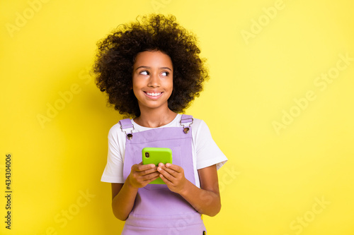 Photo of small girl hold phone look empty space wear purple overall isolated yellow color background
