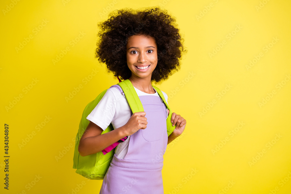 Photo of optimistic cute curly girl wear rucksack t-shirt isolated on yellow color background Photo of optimistic cute curly girl wear rucksack t-shirt isolated on yellow color background