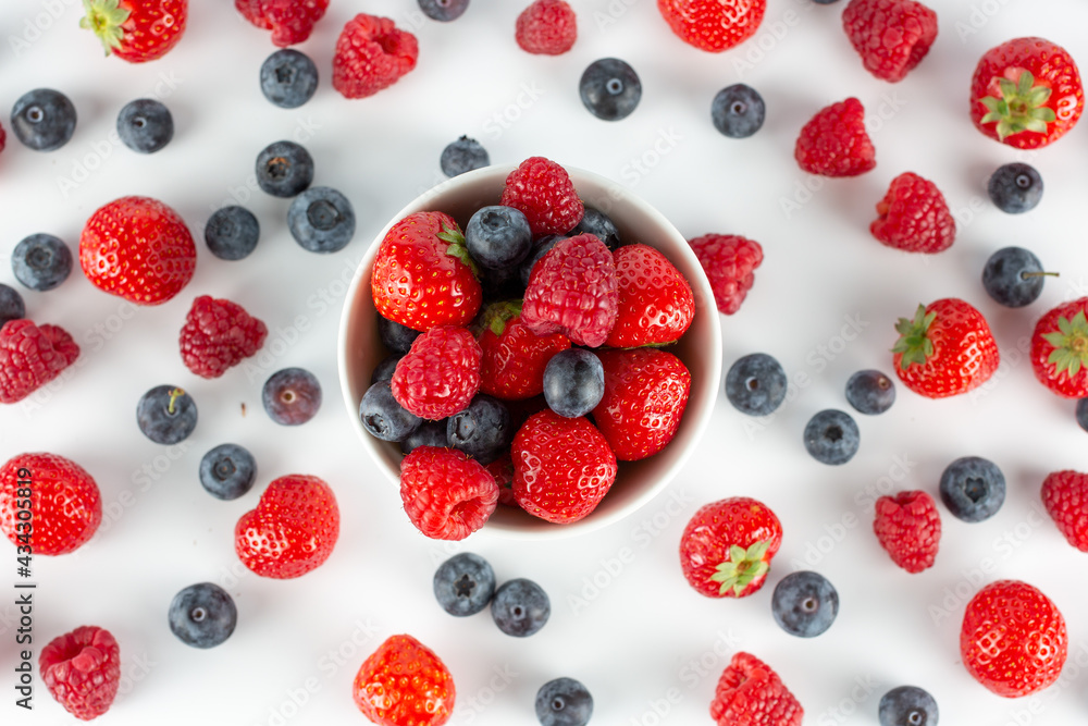 strawberries, raspberries, blueberries in a white bowl on a white background top view, with a lot of berries on the background strawberries, raspberries, blueberries in a white bowl on a white background top view, with a lot of berries on the background