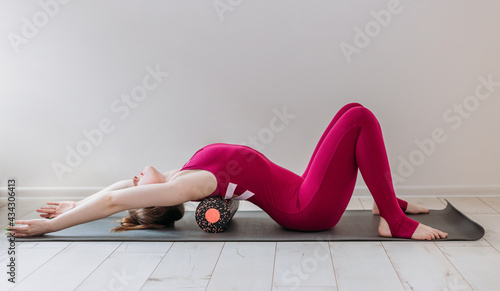 Beautiful woman pilates instructor stretching and warming up using foam roller, working out, wearing pink sportswear, close up. Sport and healthy active lifestyle concept. photo